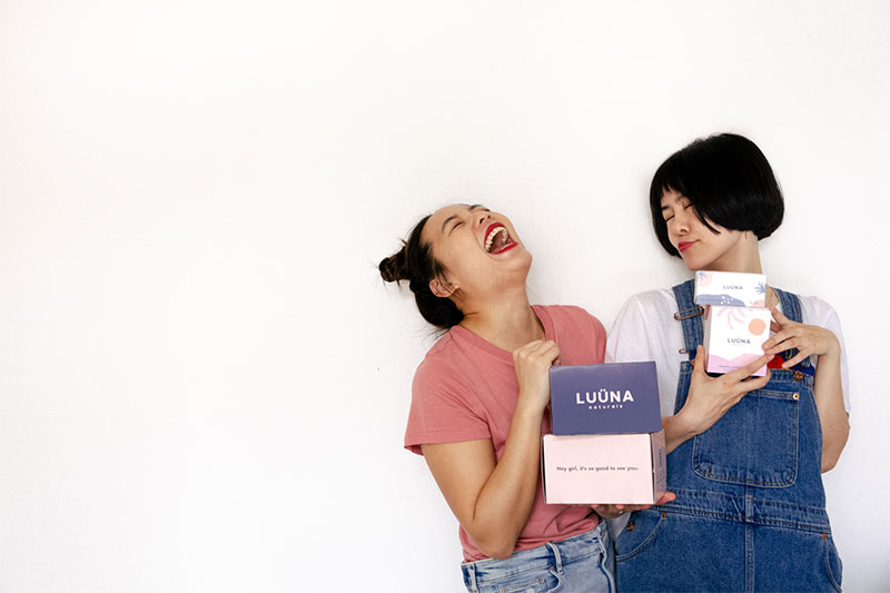 Luüna Naturals Girls Laughing Holding Boxes of Sanitary Pads Menstrual Products