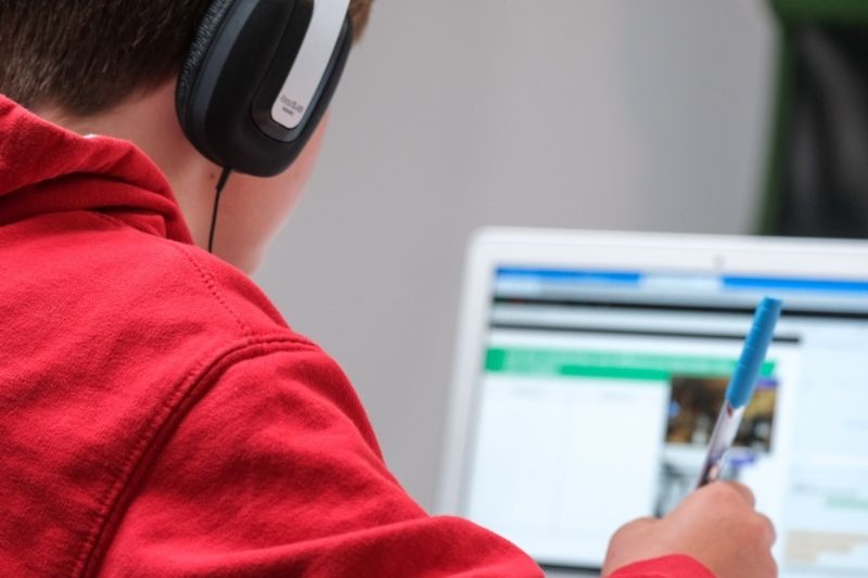 boy using headphones and computer holding pen edtech