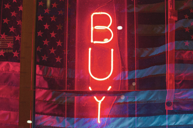 the word BUY in red neon over the american flag